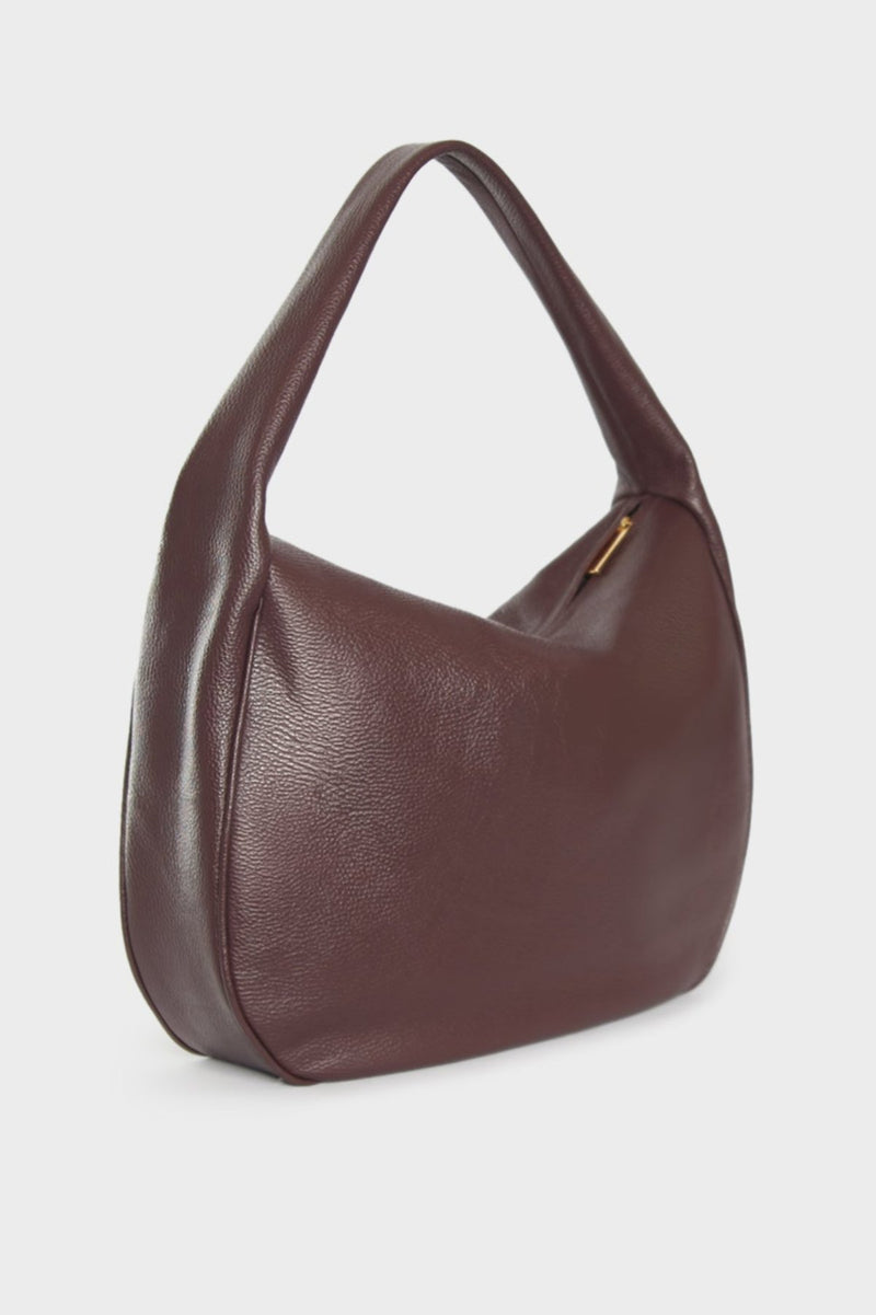 An angled image of the burgundy shoulder bag featuring its large slim body. The bag is called Slimline Halo Shoulder Bag in Grain Burgundy.