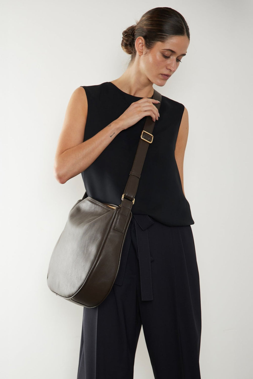 A woman wearing a crossbody bag slung across her body. It shows a side angle of the satchel showcasing its large but slim body. It can carry everyday essentials and can be used as a work bag or a travel bag.