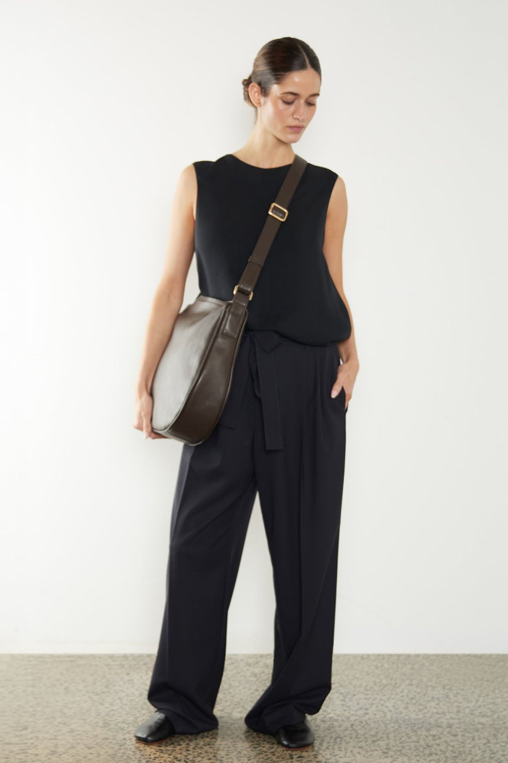 A woman wearing a crossbody bag slung across her body. It shows a side angle of the satchel showcasing its large but slim body. The bag is called Saddle Large Crossbody Bag in Smooth Dark Brown.