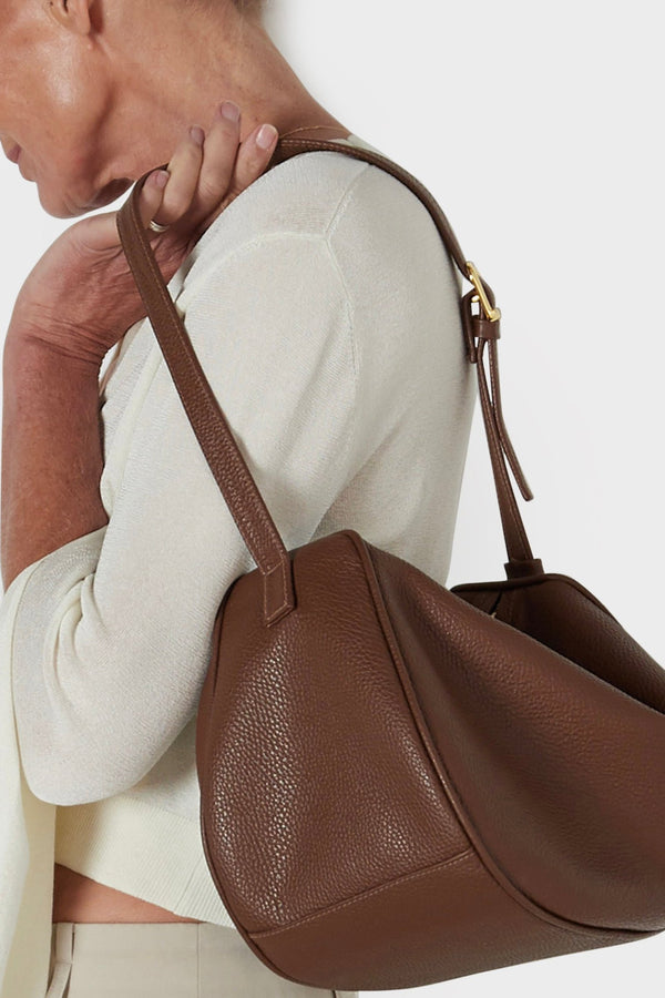 A woman holding the shoulder bag on its strap. The bag has a soft slouch and spacious body with fine stitching.