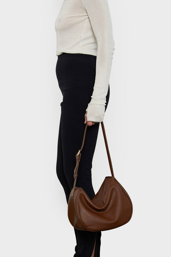 A woman holding the saddle shoulder bag in its strap. It shows the front angle of the bag with its spacious body suited as a work bag.