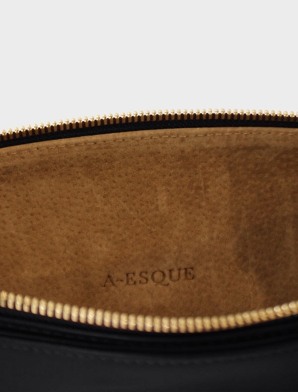 The slimline clutch pouch has a tan suede interior lining with an A-esque logo pressed on the leather. The clutch is a designed to look like a wallet or a slim purse and  features a gold hardware zipper. 