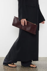 A woman carrying the red slimline clutch pouch. The clutch is folded and looks like a long wallet. It's suited as a party clutch or a casual pouch or purse.