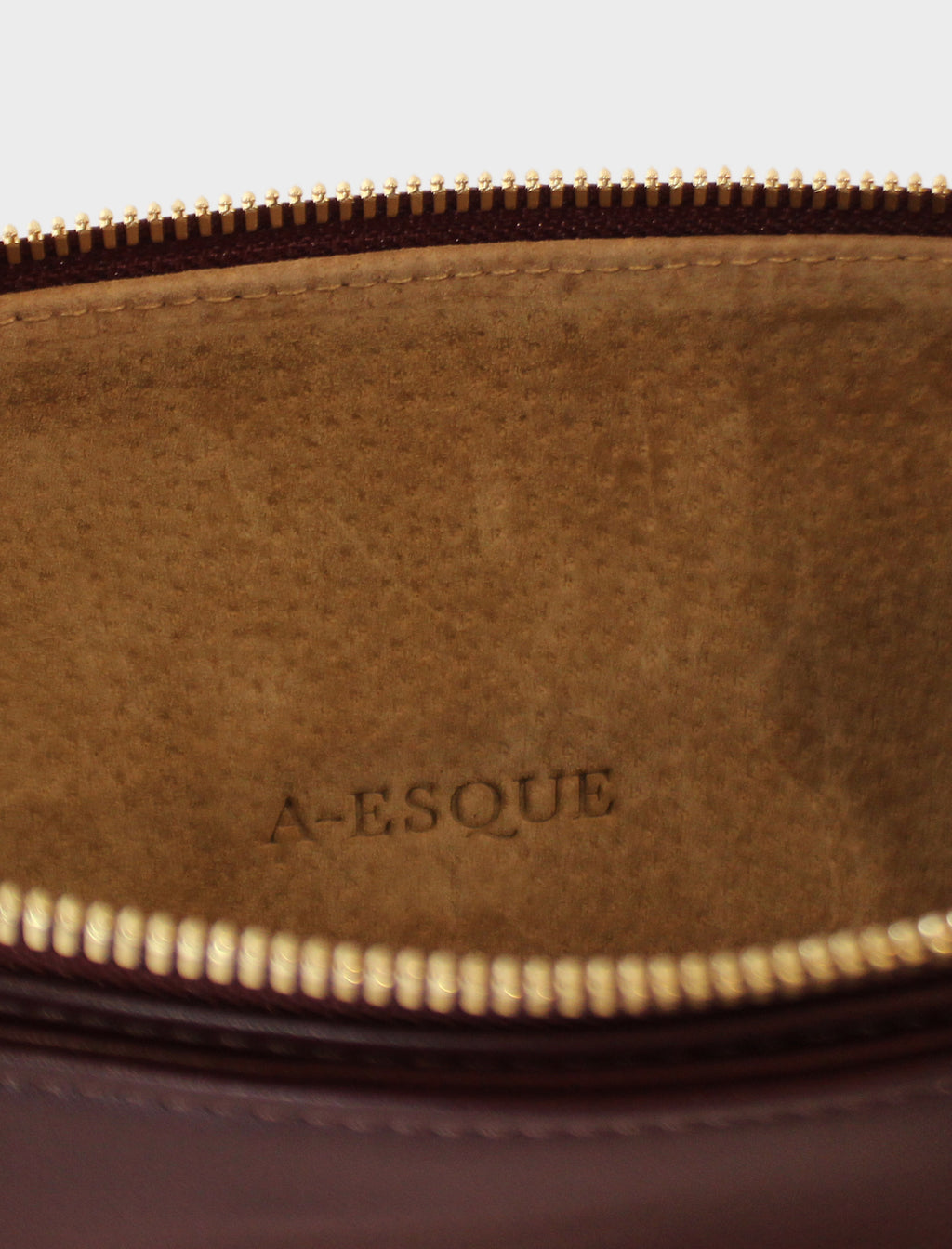 The slimline clutch pouch has a tan suede interior lining with an A-esque logo pressed on the leather. The clutch is a designed to look like a wallet or a slim purse and  features a gold hardware zipper. 