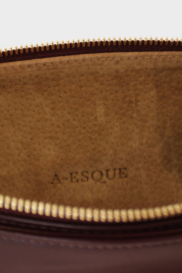 The slimline clutch pouch has a tan suede interior lining with an A-esque logo pressed on the leather. The clutch is a designed to look like a wallet or a slim purse and  features a gold hardware zipper. 