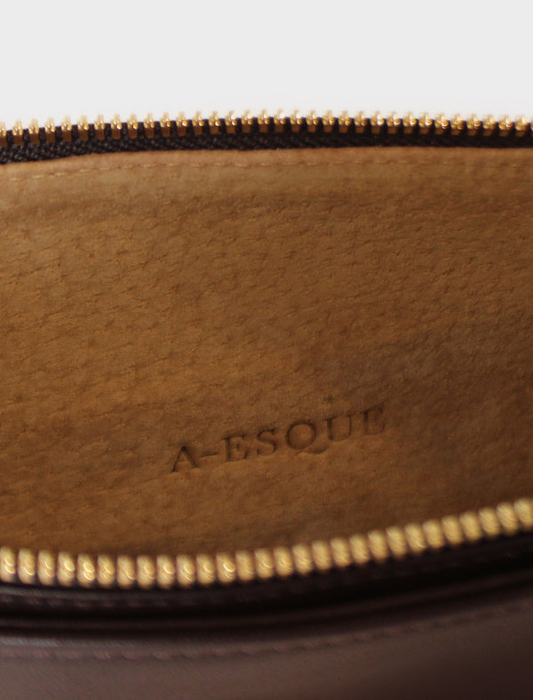 The slimline clutch pouch has a tan suede interior lining with an A-esque logo pressed on the leather. The clutch is a designed to look like a wallet or a slim purse and  features a gold hardware zipper. 