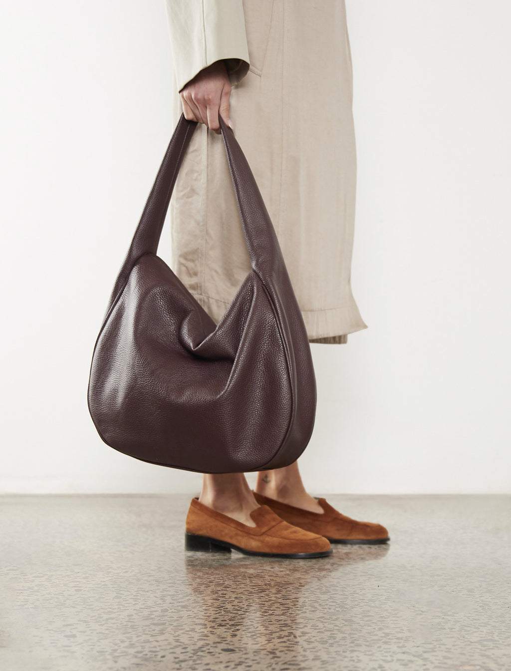 The large saddle shoulder bag in burgundy is carried handheld with its soft slouch and slim silhouette the satchel inspired bag is suited as  a work bag or a travel bag.