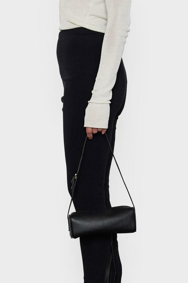 A woman holding the small black barrel shoulder bag in its handles. It highlights the elongated yet small and compact design of the handbag.