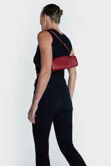 A woman carrying the small red barrel shoulder bag. It highlights the elongated and small compact design of the handbag.