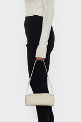 A woman holding the small white barrel shoulder bag in its handles. It highlights the elongated yet small and compact design of the handbag.