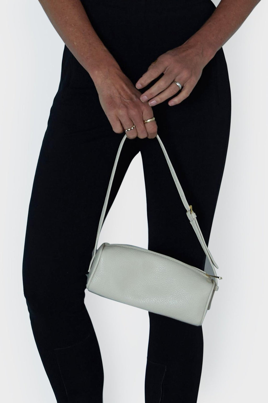 A woman holding the small white barrel shoulder bag in its handles. The handbag features an adjustable strap handles. 