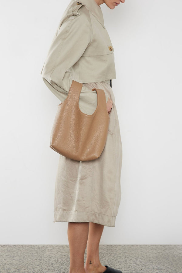 A woman carrying the beige reversible small handbag slung in the crook of the arm. This mini bag suits as a casual everyday purse bag.