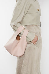 A woman carrying the pastel pink small reversible handbag slung in the crook of the arm. This mini bag suits as a casual everyday purse bag.