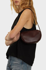 A woman wearing a small saddle shoulder bag. It features an adjustable shoulder strap in gold hardware.