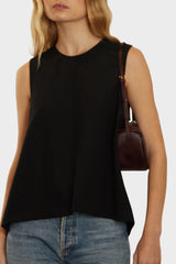 A woman wearing a small saddle shoulder bag. It shows the side of the bag with its fine hand stitching.